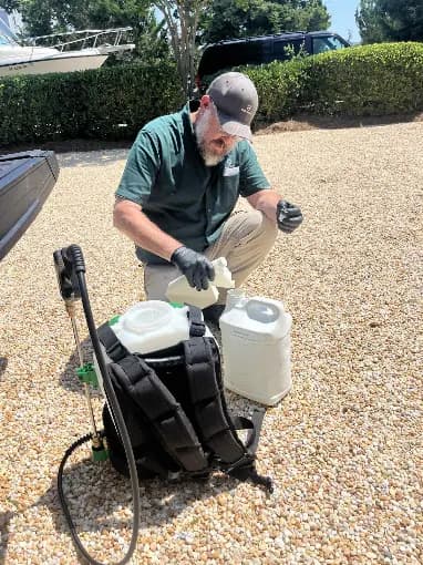 A G's Pest Control technician kneeling beside a backpack sprayer, mixing product before a treatment